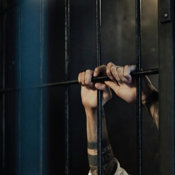 Close-up of hands holding metal prison bars, illustrating confinement and punishment.
